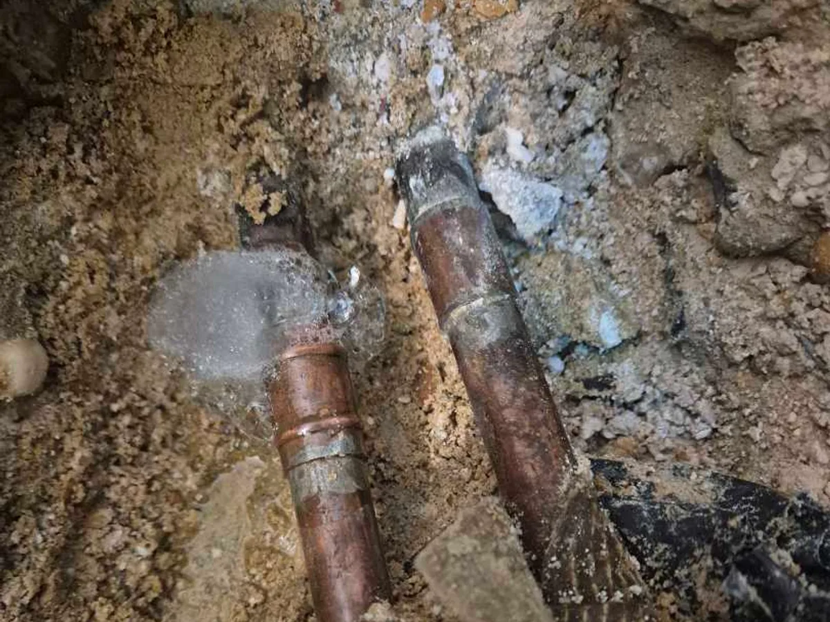 The failed soldered fitting on the heating pipe, water pooling around it in the opened floor